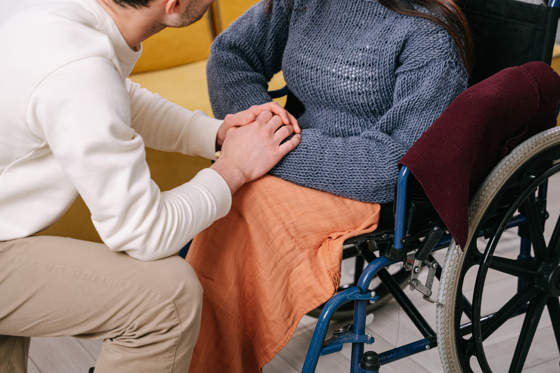 Un home agafa les mans d'una dona que està asseguda en una cadira de rodes.