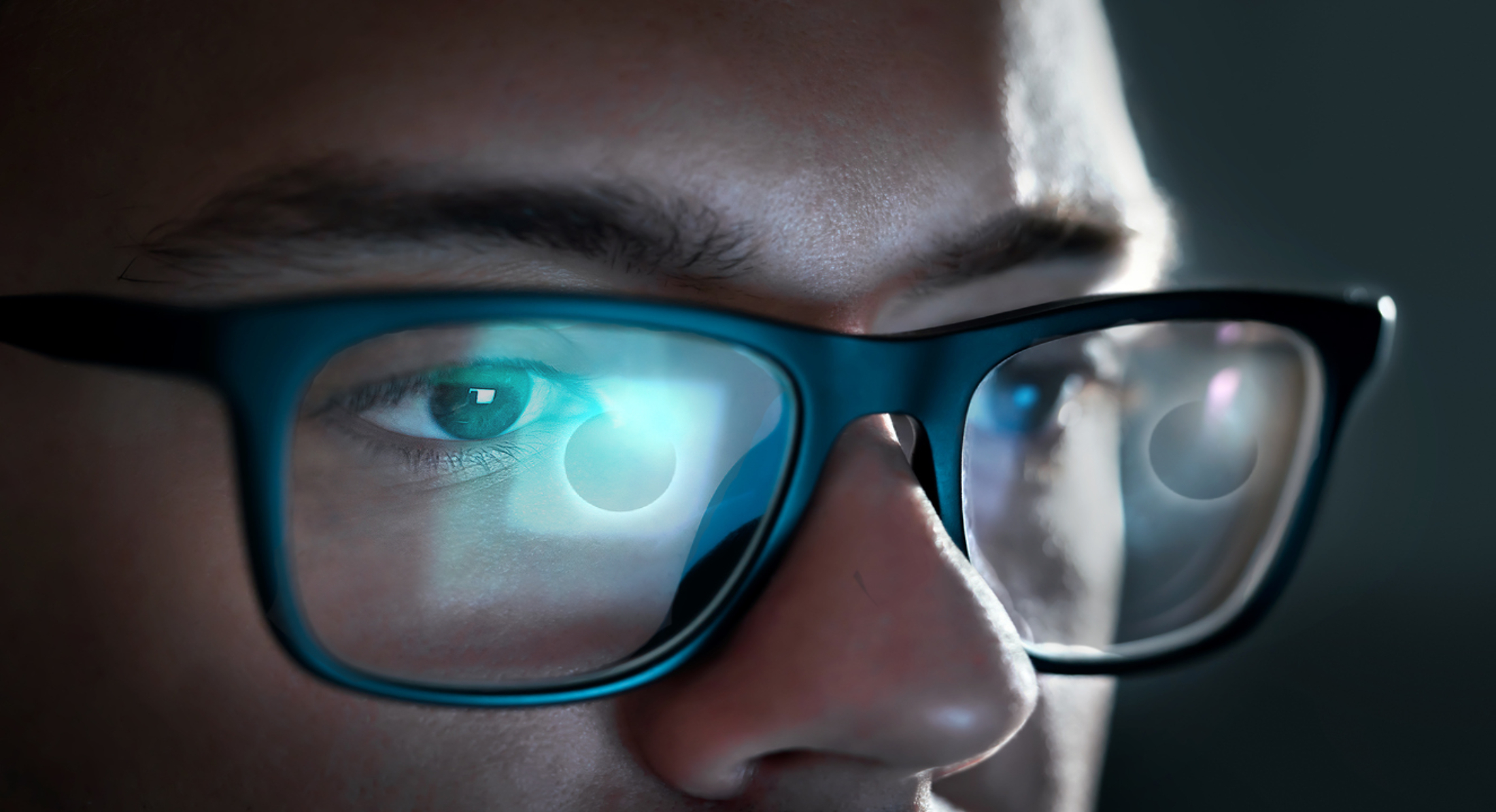 La pantalla d'un ordinador amb un eclipsi de sol es reflexa a les ulleres d'un jove.