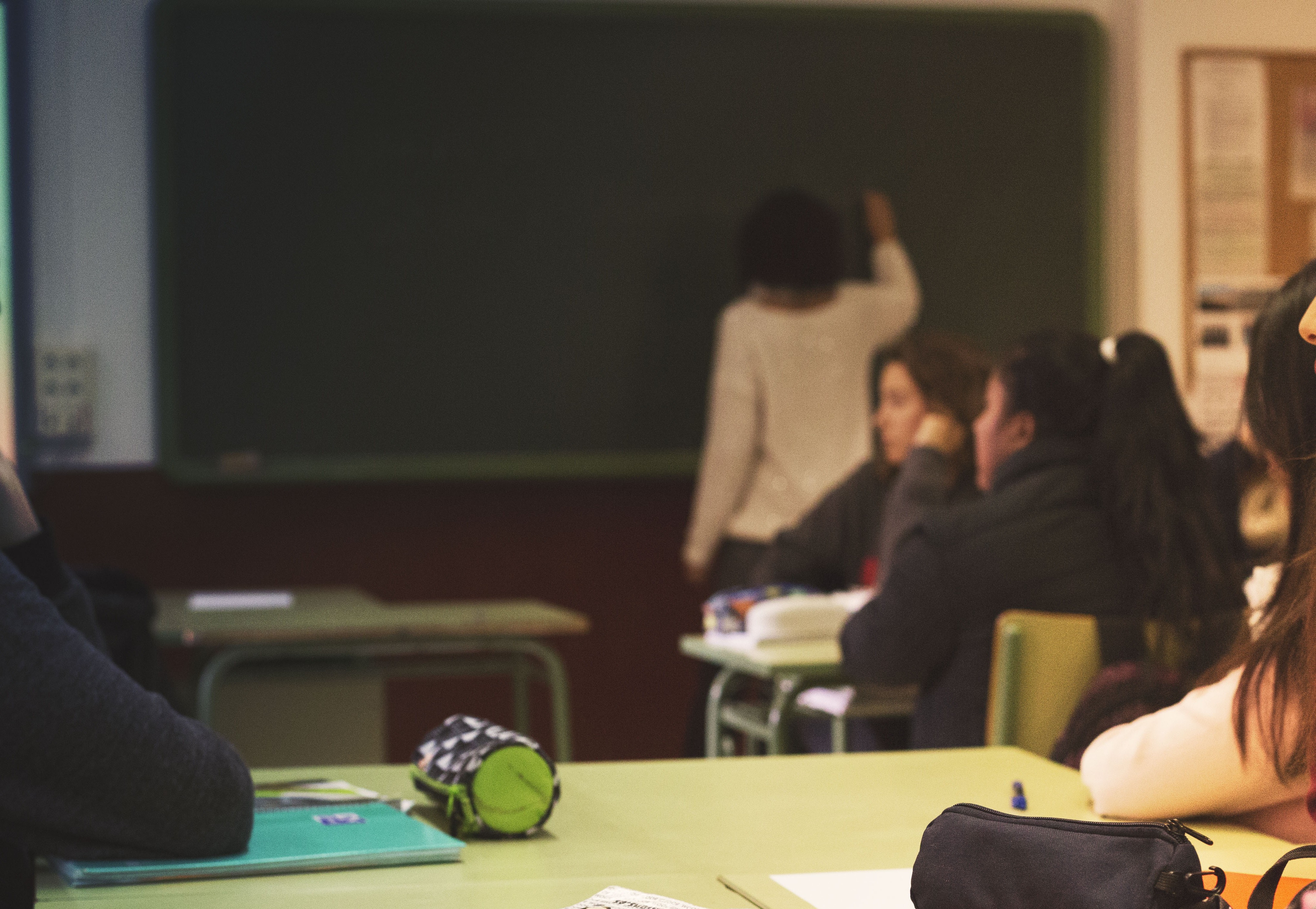 Una docent escriu en una pissarra d'una aula, on hi ha alumnes joves.