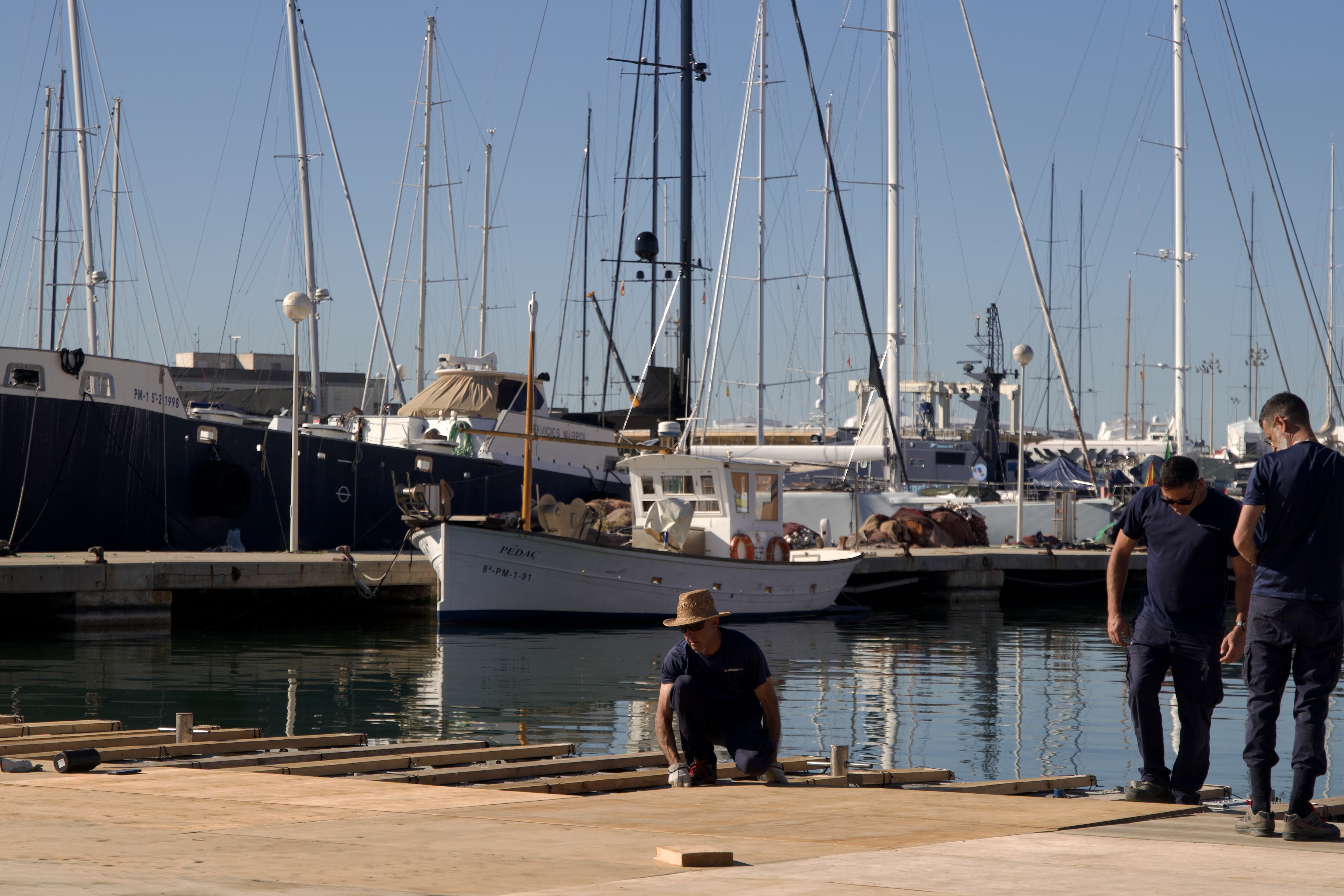 Tres operaris treballen en una plataforma de fusta al costat del moll.