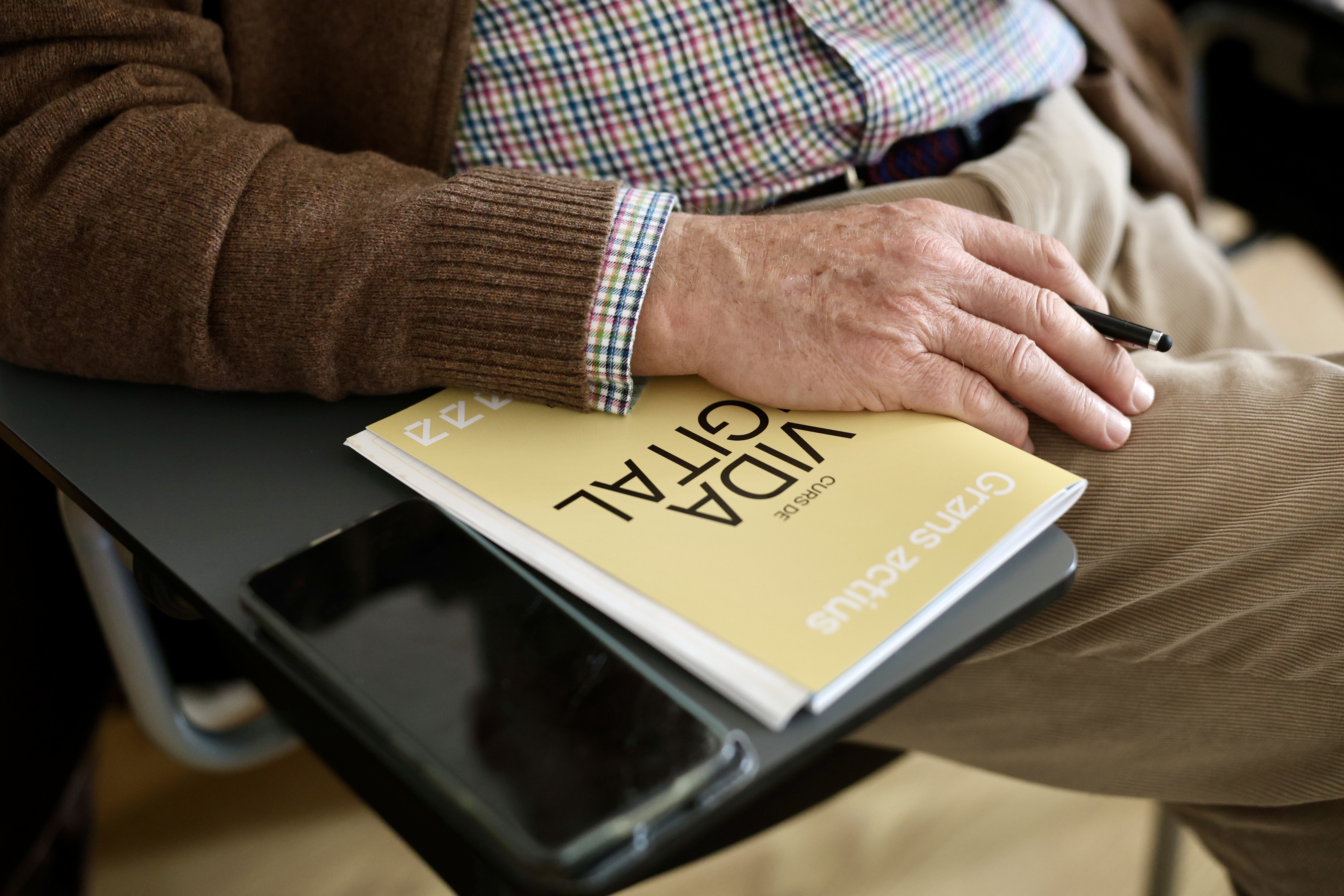 Un home gran, amb un llibre i un llàpis, seu a una cadira 