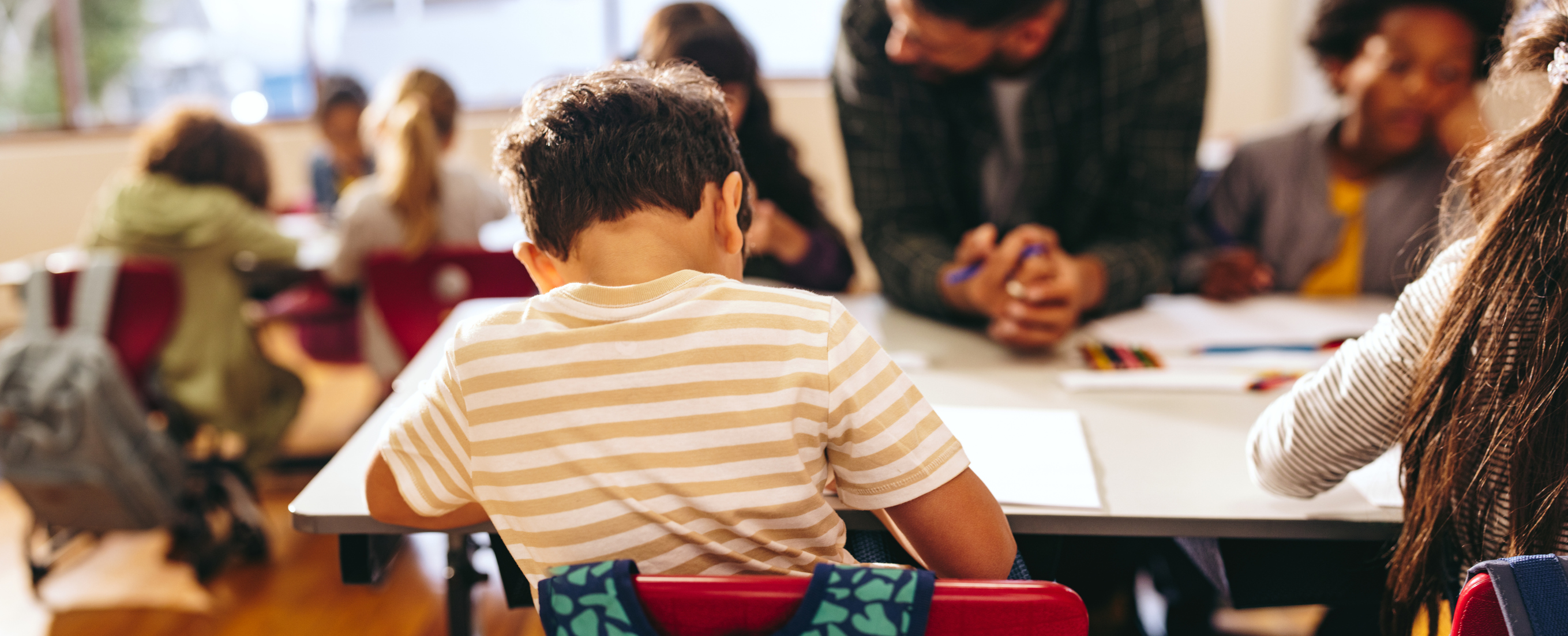 Un nin, d'esquenes, dins una aula. 